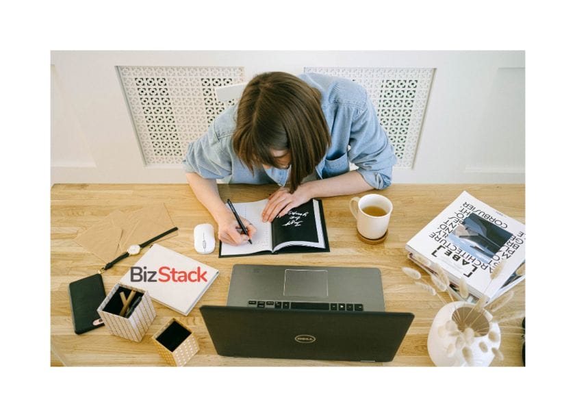 A woman taking some notes on a notebook in front of a laptop.