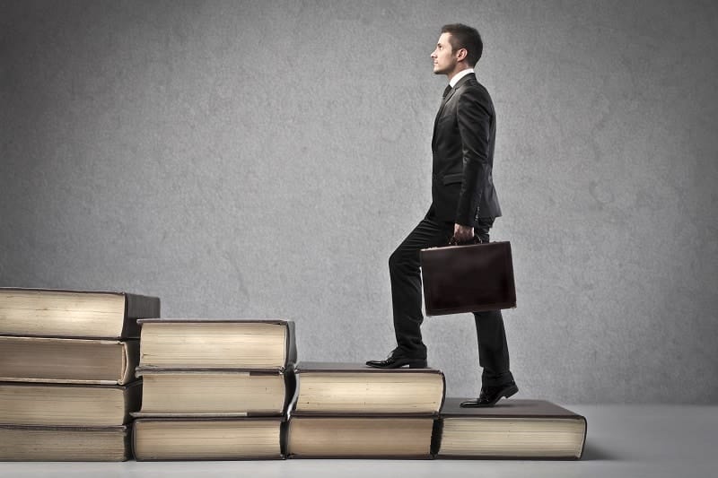 A male entrepreneur in a suit is climbing a stack of books.