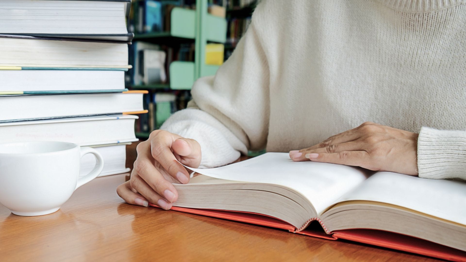 A woman is reading a book from a stack of books, possibly searching for the best book for new entrepreneurs.
