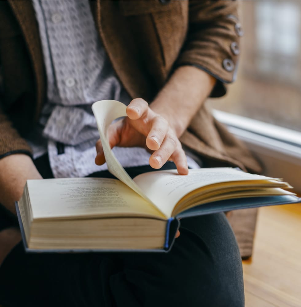 A man reading one of the best finance books for entrepreneurs in front of a window.