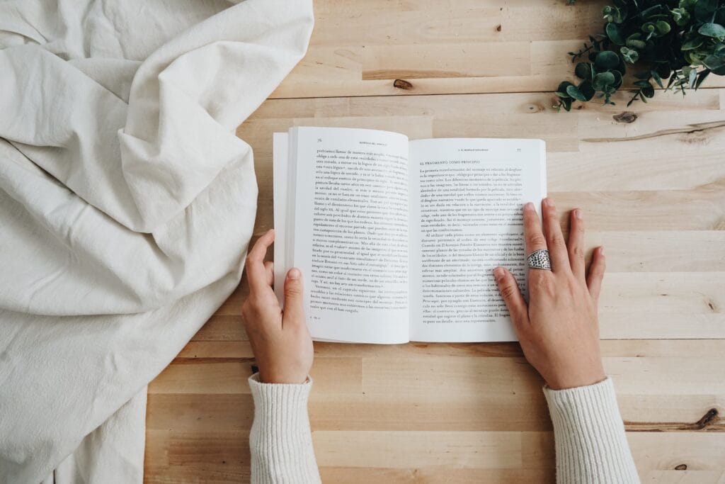 A woman is reading one of the best books for creative entrepreneurs on a wooden table.