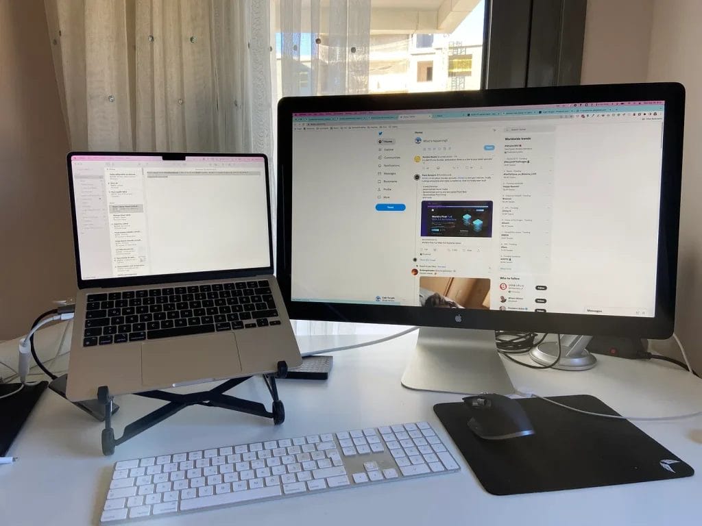 A dual-monitor workstation setup, featuring a laptop on a stand and a separate monitor, with an external keyboard and mouse.