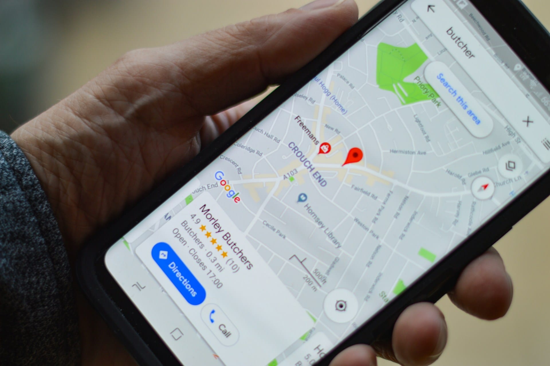 Person holding black smartphone and looking at a butcher search result on Google Maps, highlighting a local butcher in the area.