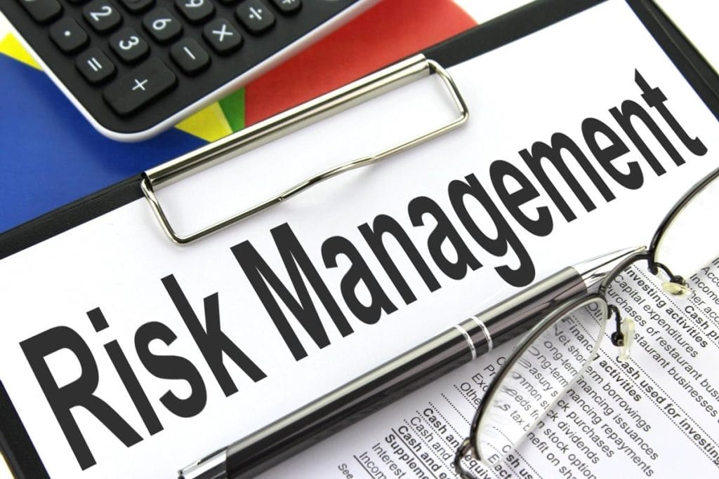 A clipboard with the words "Risk Management," a pair of eyeglasses, a pen, part of a calculator, and a multicolored background symbolize the role of AI in crisis management for ensuring business continuity during crises.